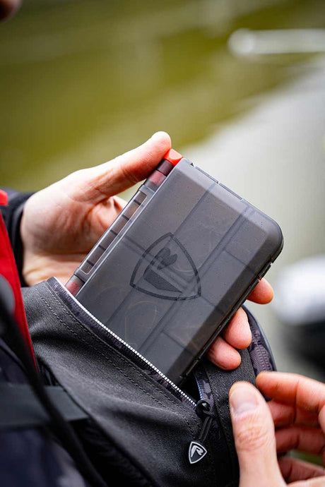 Caja de accesorios Fox Rage Mediana guardada en un bolsillo, ideal para pesca de bass y depredadores.